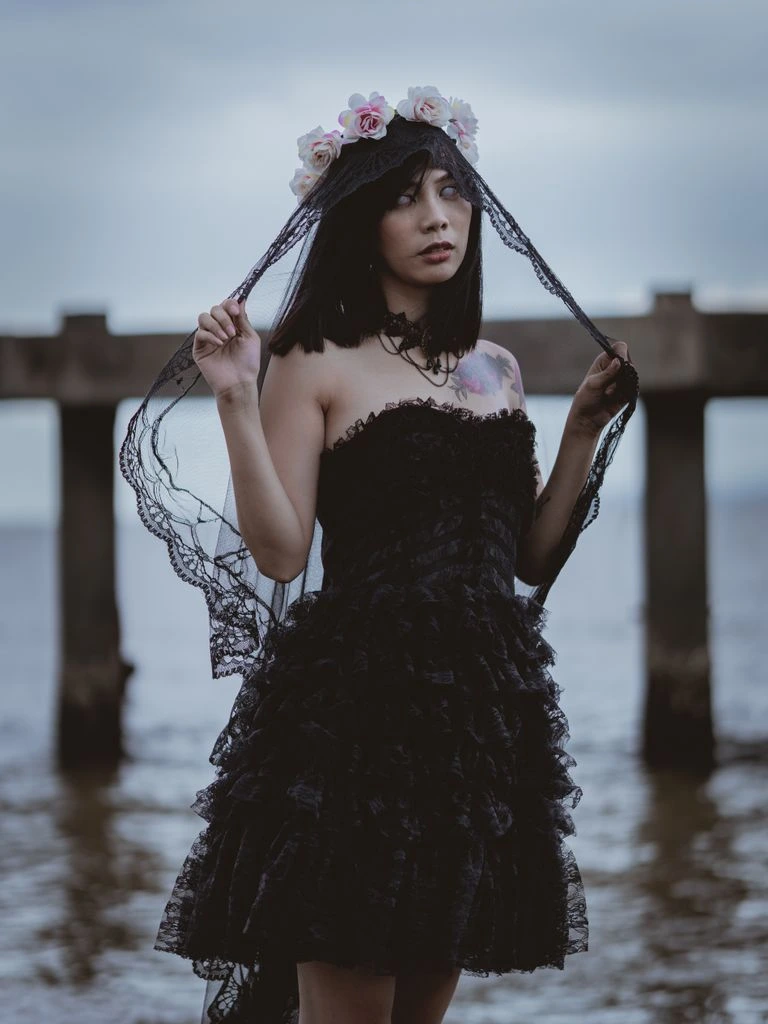 A bride in a black high-neck crepe gown with architectural shoulders stands in a converted industrial loft with dramatic window light.